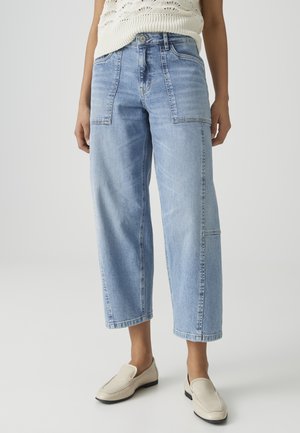 Vrouw draagt lichtblauwe, wijde cropped jeans met voorzakken, off-white gebreide mouwloze top en crèmekleurige loafers.