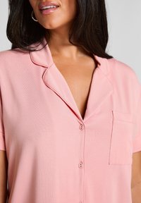 Lichtroze overhemd met korte mouwen en knopen, met een borstzak en een zachte textuur, een soepele kraag en subtiele details.