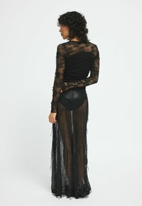 Schwarzes Netzkleid mit langen Spitzenärmeln, figurbetonter Oberteil und transparenter Rock mit Fransenverzierungen und vertikalen Streifen.