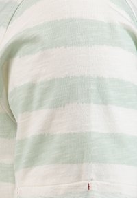 Primo piano di tessuto che mostra un maglione morbido con ampie strisce orizzontali nei colori verde pallido e bianco sporco.