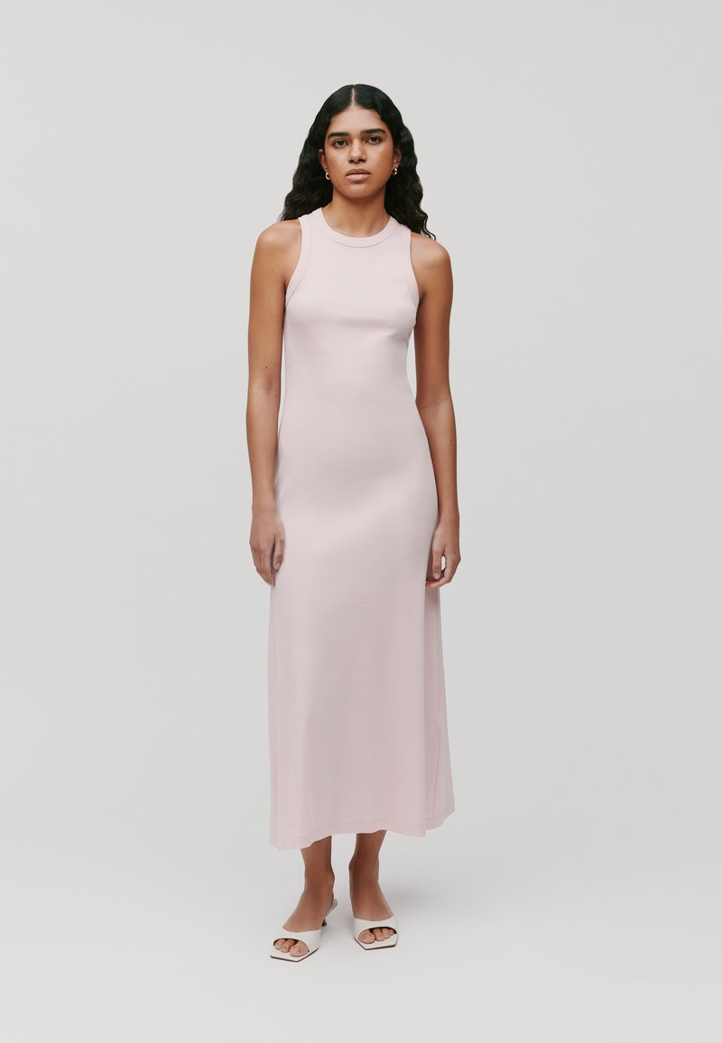 Mouwloze roze midi-jurk van een soepel stof met een aansluitende silhouette. Geaccentueerd door een ronde hals en een minimalistisch ontwerp, gecombineerd met witte instap-schoenen.