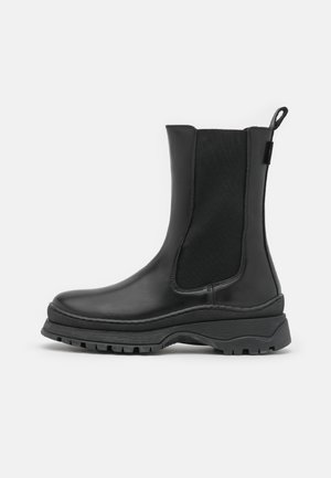 Bottillons en cuir noir avec des panneaux élastiques sur les côtés, semelle épaisse et texturée, et une languette à l'arrière pour un enfilage facile. Fini lisse et construction durable.