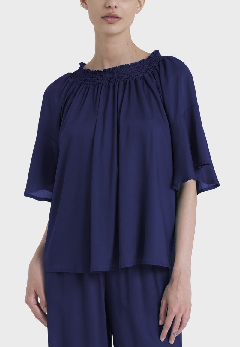 Blusa blu navy con scollatura arricciata, maniche a farfalla corte e vestibilità morbida, realizzata in un tessuto leggero.