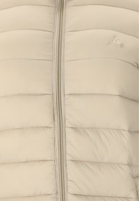 Beige pufferjakke med horisontalt quiltet design, glat tekstur, central lynlås og et diskret logo på brystområdet.