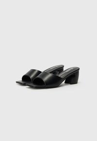 Schwarze High-Heel-Mules mit offenem Zeh, aus glattem synthetischem Material gefertigt. Merkmale sind eine quadratische Form und ein blockiger Absatz.