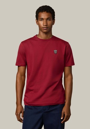Rotes T-Shirt mit kurzen Ärmeln aus Baumwollmischung, Rundhalsausschnitt, mit einem kleinen schwarz-weißen Logo auf der Brust, glatte Textur, lockere Passform.