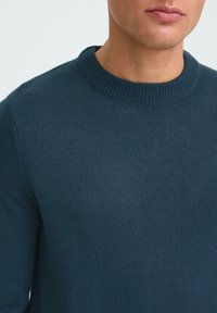 Donkerblauwe gebreide trui met ronde hals, voorzien van geribde manchetten en zoom, en een zachte textuur. Geen zichtbare patronen of hardwaredetails.
