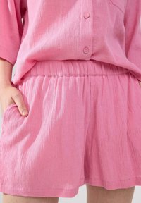 Lös passform rosa outfit gjort av texturerad tyg, med en knapp-up topp och shorts med elastisk midja och sidfickor.