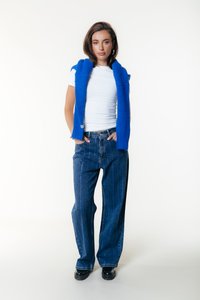Chaleco de punto azul llevado sobre una camiseta blanca, combinado con jeans de mezclilla oscura de pierna ancha que cuentan con rayas verticales. Calzado negro.