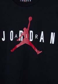 Camiseta de algodón negra con una gran silueta roja de un jugador de baloncesto en el aire y el texto "JORDAN" en letras blancas en negrita.