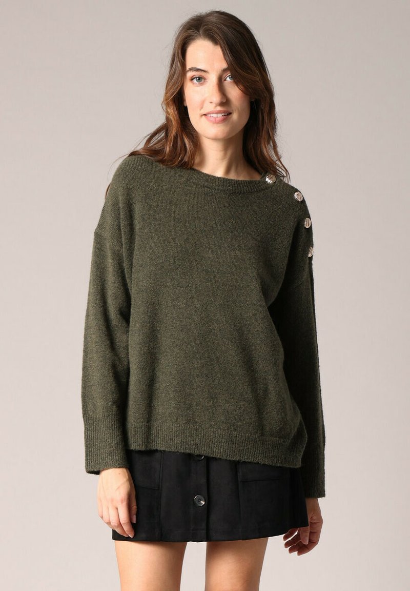 Pull en maille vert olive avec un décolleté large et des épaules tombantes. Présente des boutons décoratifs sur l'épaule gauche et une coupe décontractée.