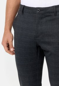 Pantalones de cuadros gris oscuro a medida con acentos azules, confeccionados en tejido texturizado. Presentan un cierre frontal con botón y bolsillos laterales.