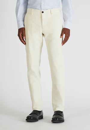Crème kleurige corduroy broek met een rechte snit, voorzakken en een enkele zwarte knoopsluiting, gecombineerd met zwarte schoenen en een gestreept shirt.