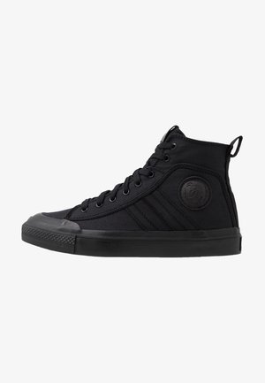 Zapatilla de lona negra de caña alta con cordones en la parte delantera, suela de goma y parche circular con logo en la zona del tobillo.