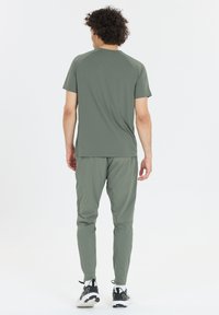 Grön sportt-shirt med korta ärmar och matchande tapered byxor, tillverkade av lätt material. Svarta sneakers med vita detaljer.