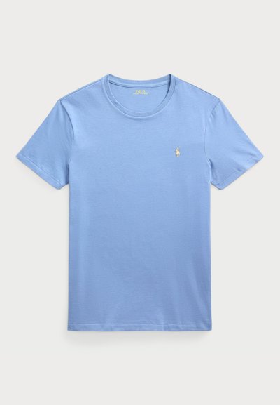 Gaiši zils kokvilnas T-krekls ar apaļu kakla izgriezumu, īsām piedurknēm un nelielu dzeltenu logo kreisajā krūtī. Gluda tekstūra.