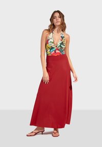 Květinový halterneck top s hlubokým výstřihem do V, spárovaný s dlouhou, splývavou červenou sukní. Oblečení má hladké textury a štíhlé ramínka.