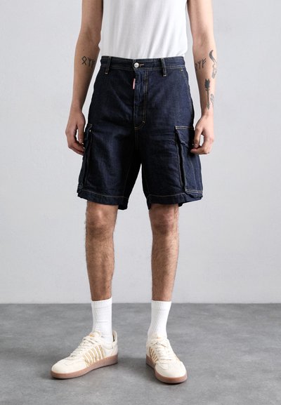 Dunkelblaue Denim-Shorts mit Cargo-Style und umgeschlagenen Säumen, ausgestattet mit Vorder- und Seitentaschen, kombiniert mit weißen Socken und cremfarbenen Sneakers.