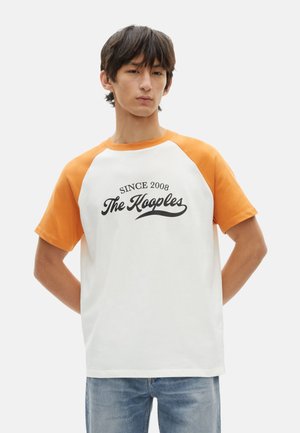 Heren t-shirt met korte oranje raglan mouwen, witte body, zwarte tekst "Sinds 2008 The Kooples," en een relaxed fit. Katoenen stof.