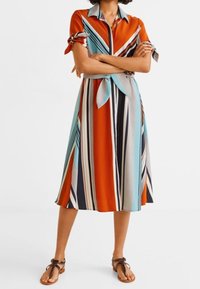 Robe chemise rayée à manches courtes, présentant des rayures orange, bleues et marine. Le matériau semble léger avec un détail de taille nouée.