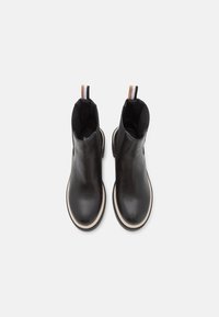 Botas de cuero negras hasta el tobillo con acabado suave, punta redondeada, suela de goma blanca y una lengüeta en la parte trasera a rayas marrón y blanca.
