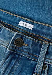 Džínové kalhoty v středně modré barvě s měděným prošíváním. Obsahují kovový knoflík s textem "TWO SOON JEANS" a látkovou štítku s velikostí 32/32.