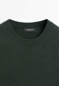 Donkergroen trui met een geribbelde ronde halslijn, zachte textuur en een label met de tekst "Massimo Dutti." Gemaakt in China.