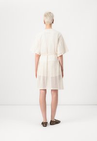 Rochie tricotată crem, cu mâneci deschise și talie accentuată, având un model texturat în zigzag și o lungime până la genunchi.