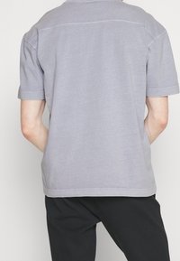 Harmaa lyhythihainen t-paita, rento istuvuus, pyöreä pääntie ja suora helma. Pehmeä kangas, jossa on vain vähän sauman yksityiskohtia takana.