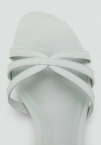 Sandalette verde deschis, cu trei curele subțiri, care se încrucișează. Textură netedă, cu un design minimalist și o talpă plată.