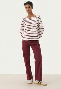 Maglione a maniche lunghe a righe in crema e bordeaux, abbinato a pantaloni dritti bordeaux. Il modello indossa sneakers bianche con dettagli neri.