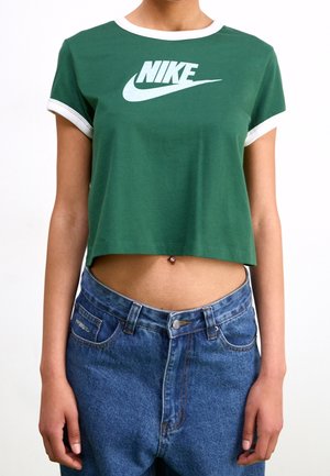 Groene cropped t-shirt met witte ribbelkraag en manchetten, met een groot wit Nike-logo op de voorkant. Draagt een hoge taille blauwe spijkerbroek.