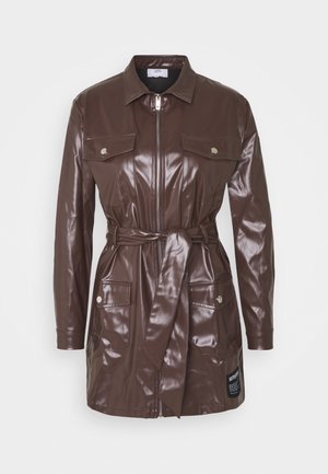 Chaqueta de manga larga de imitación de cuero marrón con cremallera en la parte delantera, cinturón en la cintura, cuatro bolsillos con solapa y botones, y un pequeño parche negro cerca del dobladillo.