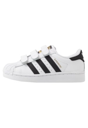Baskets blanches Adidas Superstar avec trois bandes noires, trois bandes blanches en velcro et texte doré "Superstar" sur le côté.