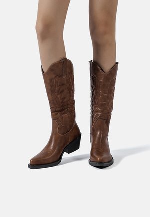 Stivali da cowboy in cuoio marrone con punta appuntita, cuciture decorative e tacco a blocco di media altezza, caratterizzati da un design impresso sul gambale.