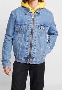 Ljusblå denimjacka med lång ärm, dragkedjestängning fram, två bröstfickor och en något kortare passform. Har kontraststickning.