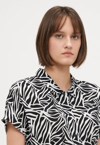 Crna i bijela majica kratkih rukava s uzorkom zebra pruga, s kragnom i dugmadima sprijeda. Mekana, lagana tkanina.