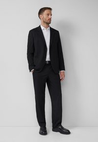 Schwarzer Anzug mit einer Slim-Fit-Jacke und passenden Hosen, kombiniert mit einem weißen Hemd. Lederschuhe vervollständigen den formellen Look.