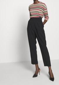 Svetr s proužkovaným rib pletením červené, zelené a béžové barvy, v kombinaci s černými kalhotami s vysokým pasem. Celkový vzhled doplňují černé lodičky na vysokém podpatku.