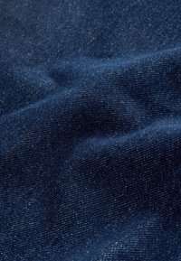 Tessuto di denim blu navy con superficie leggermente strutturata, caratterizzato da sottili variazioni di tonalità e dettagli intrecciati fini, liscio e flessibile.