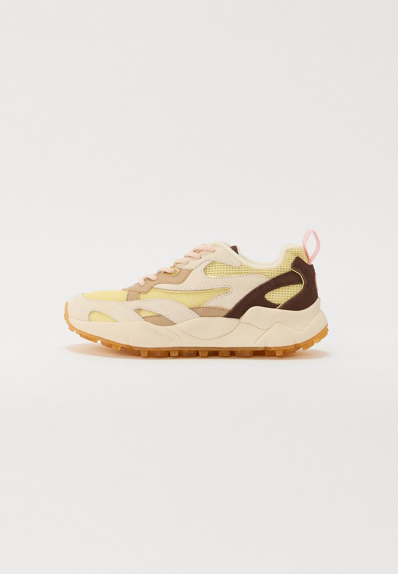 Sneakers feature a mix of beige, yellow, and brown materials, with mesh accents and a textured rubber sole. The design includes pink laces and heel tab.