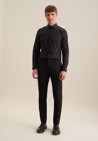 Camicia nera con colletto a punta, abbinata a pantaloni neri e scarpe nere, creando un completo formale coordinato.