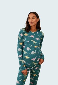 Långärmad tröja och byxor med dinosauriemönster i teal-tyg, med färgglada dinosaurieillustrationer i rosa, gult och grönt.