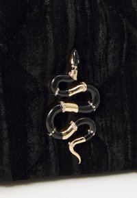 Borsa in velluto nero con un'applicazione a forma di serpente in oro e nero, arricchita da accenti di strass. Superficie texturizzata con un motivo trapuntato.