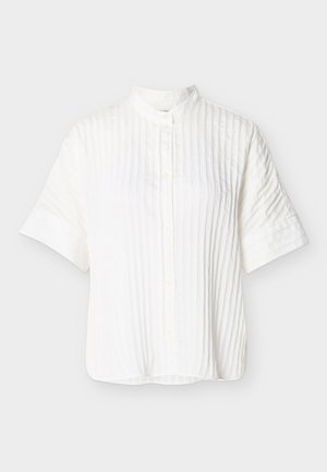 Λευκό πουκάμισο με κοντά μανίκια, κάθετες πιέτες, όρθιο γιακά και κουμπιά μπροστά, σε απλό ανοιχτό γκρι φόντο.