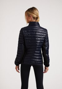 Marineblauer Puffer-Jacke mit gestepptem Design, hohem Kragen und schwarzen Seitenpanelen; glatte, glänzende Textur mit langen Ärmeln.