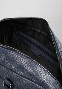 Intérieur d'un sac à main en cuir texturé bleu marine, comportant une poche zippée et un motif de logo répétitif sur un revêtement en tissu sombre.