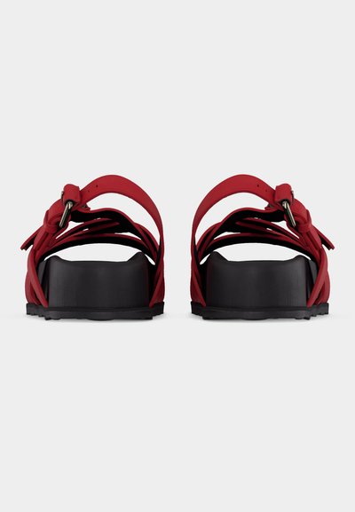 Sandales rouges à brides avec semelles compensées noires et boucles de cheville ajustables, vues de face sur un fond uni.