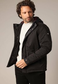 Veste noire rembourrée avec capuche amovible, fermeture éclair à l'avant et fermetures à pression. Présente un design élégant et une doublure intérieure contrastante.