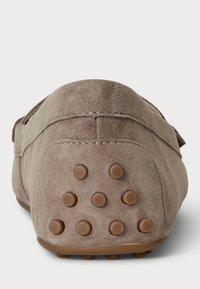 Bež semiš čevlji brez pete z zaobljenim prstom in gumijastim podplatom. Posebne značilnosti vključujejo serijo rjavih dimplastih gripov na peti.